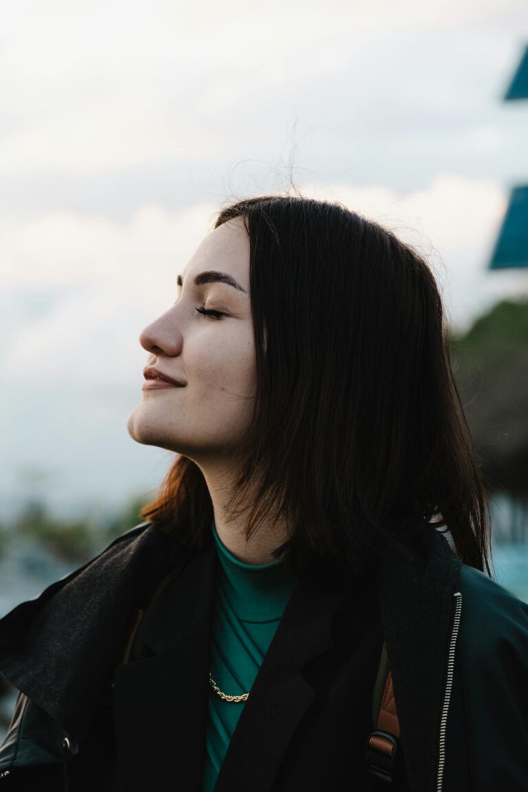 A serene outdoor portrait of a young woman with closed eyes and brunette hair, embracing tranquility.